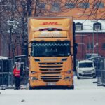 A yellow truck among snowy urban streets, surrounded by buildings and winter scenery.