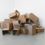 A pile of empty cardboard boxes arranged on a grey floor against a white wall, perfect for moving themes.